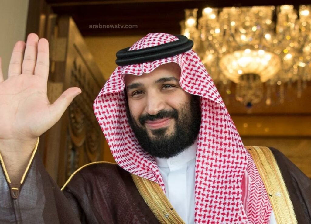 - Smiling man in traditional Saudi attire waves hello at the camera.