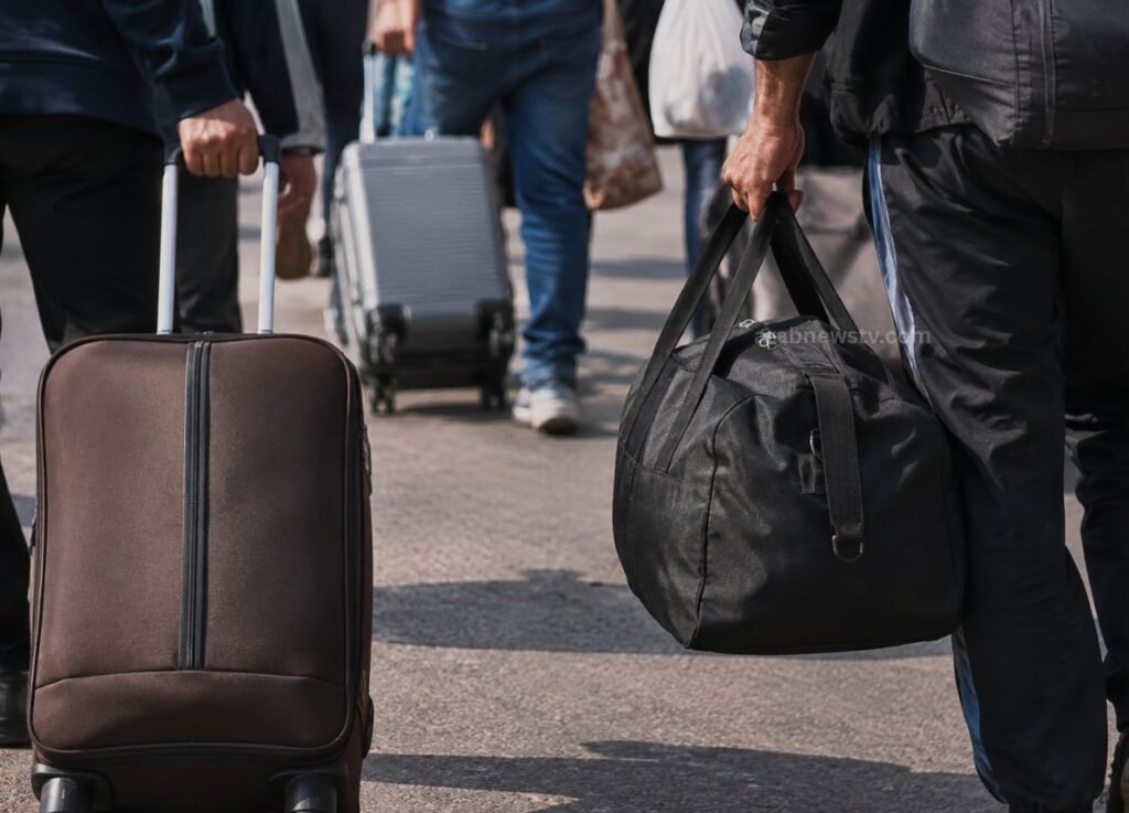 People walking with rolling suitcases and a black duffel bag in an outdoor transit area, suggesting travel.